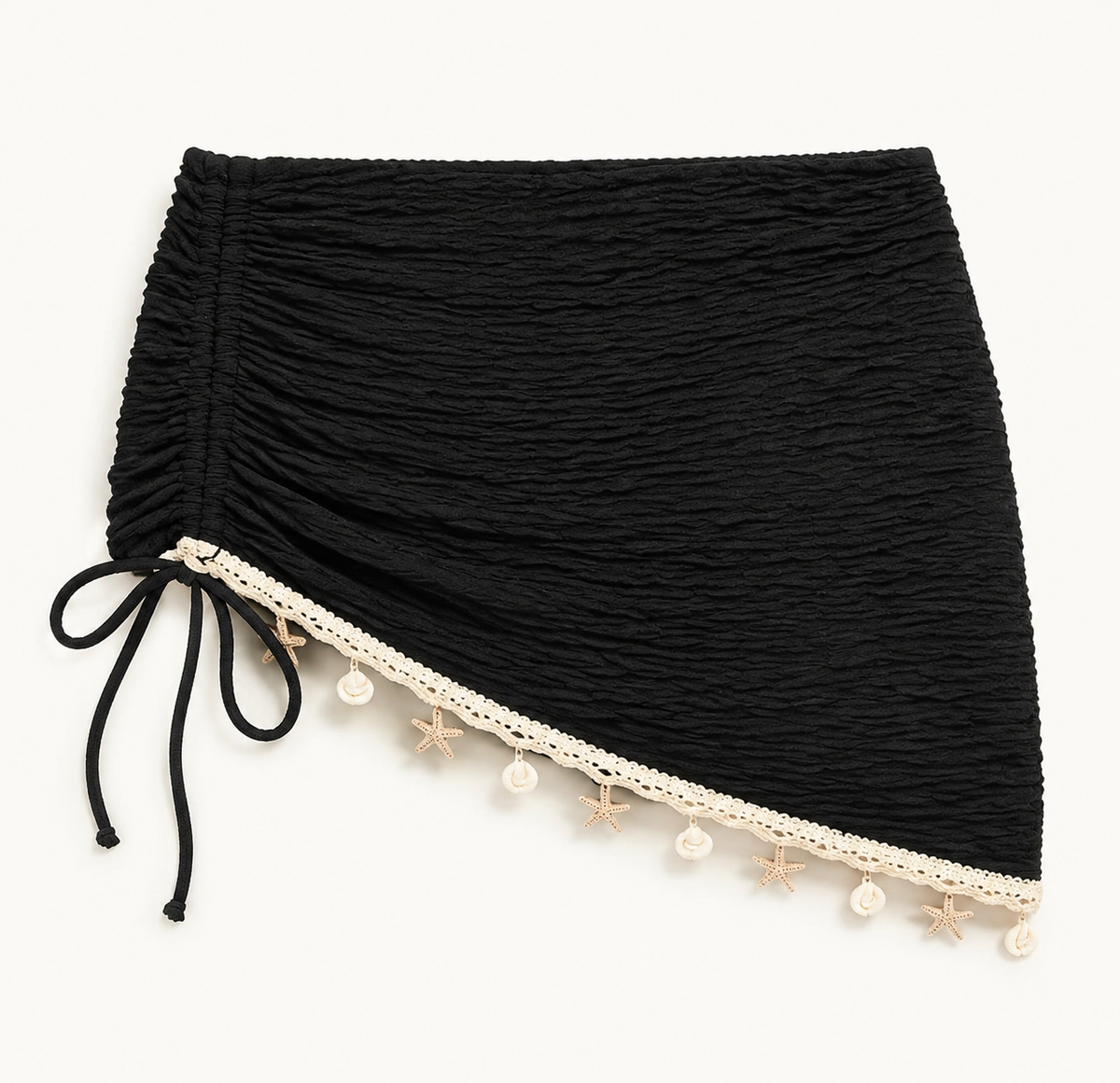 Black ruched mini cover-up detail showing the side tie, diagonal cream trim, and shell-like hem accents.
