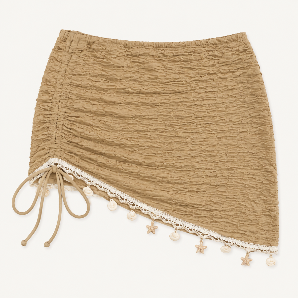 Tan-khaki ruched mini cover-up detail showing the side tie, diagonal cream trim, and shell-like hem accents.