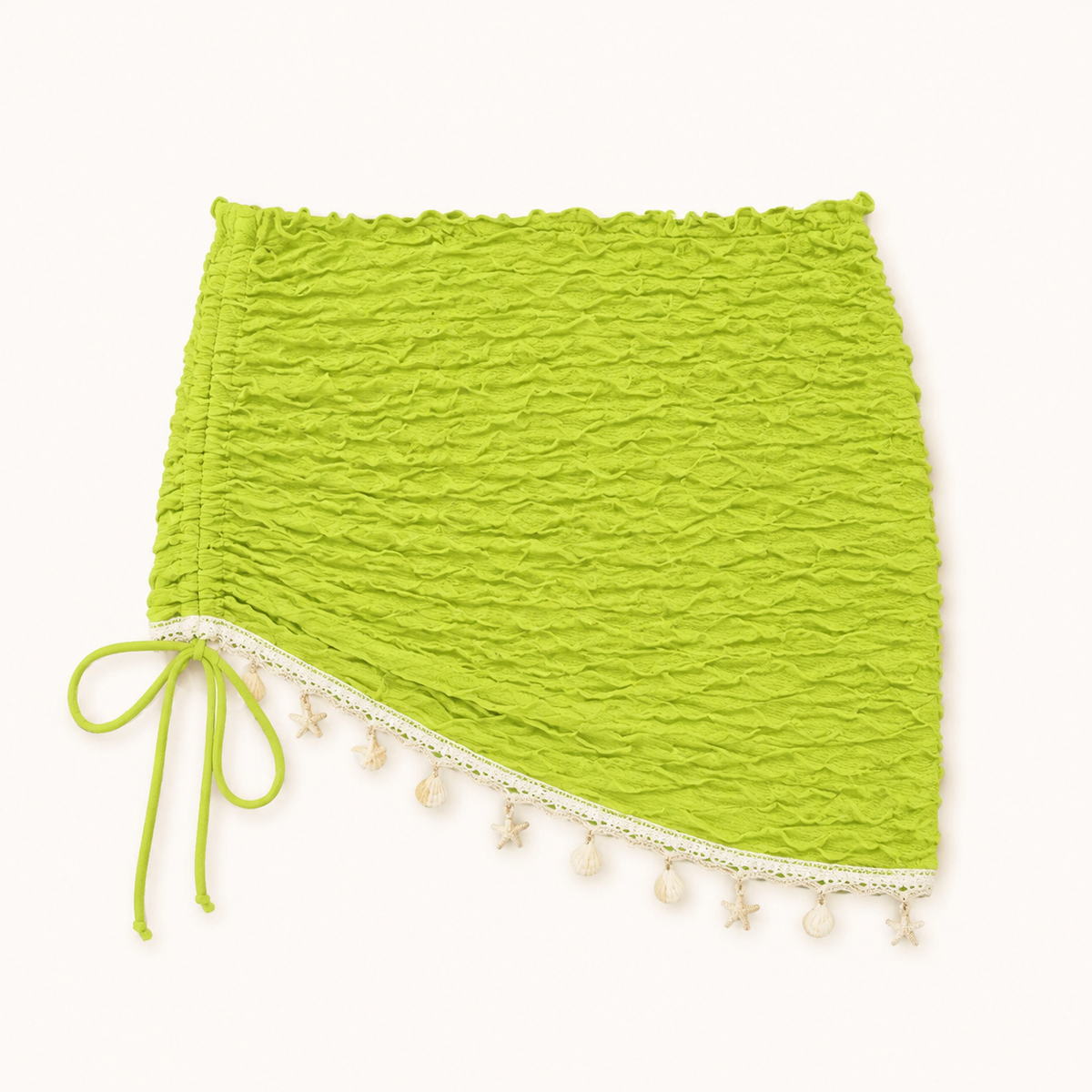 Lime-green ruched mini cover-up detail showing the matching side tie, diagonal cream trim, and shell-like hem accents.